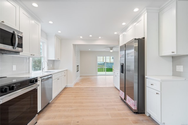 kitchen with white cabinets, appliances with stainless steel finishes, sink, backsplash, and light hardwood / wood-style flooring