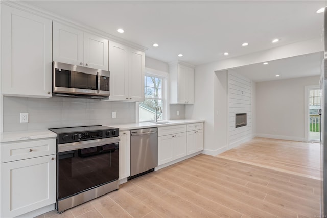 kitchen with appliances with stainless steel finishes, tasteful backsplash, a fireplace, white cabinets, and light hardwood / wood-style flooring