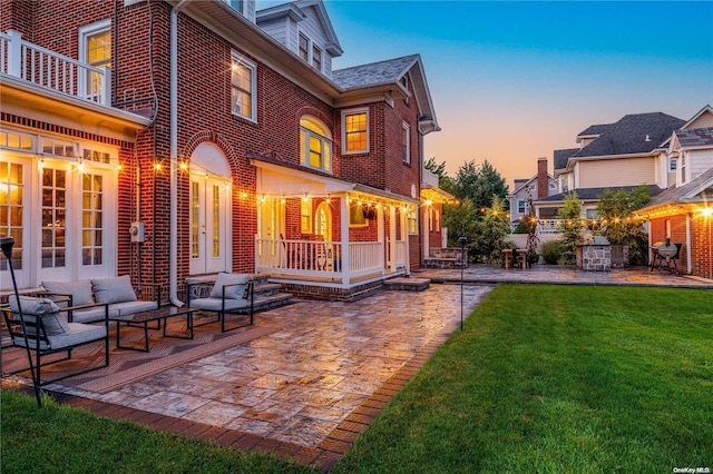 back house at dusk with a lawn, outdoor lounge area, a balcony, and a patio