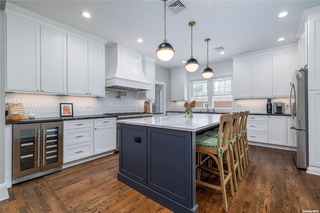 kitchen with white cabinets, appliances with stainless steel finishes, premium range hood, and beverage cooler