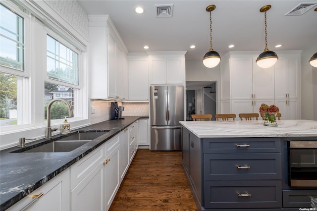 kitchen with sink, dark wood-type flooring, dark stone countertops, stainless steel fridge, and white cabinets