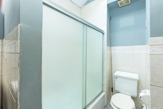 bathroom with tile walls, shower / bath combination with glass door, and toilet