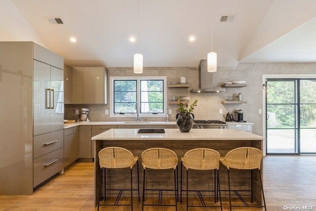 kitchen with wall chimney range hood, sink, a healthy amount of sunlight, and vaulted ceiling