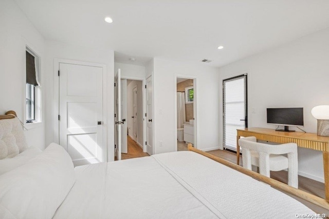 bedroom with wood-type flooring, connected bathroom, and multiple windows