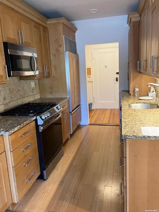 kitchen with a sink, ornamental molding, appliances with stainless steel finishes, light wood-style floors, and backsplash