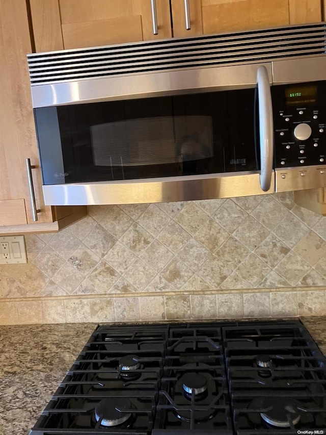 interior details with stainless steel microwave, brown cabinets, stovetop, dark stone counters, and backsplash