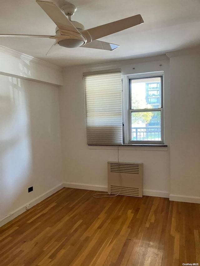 spare room with baseboards, wood finished floors, a ceiling fan, and radiator