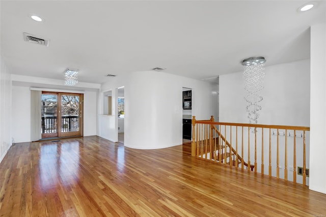 spare room with an inviting chandelier, wood finished floors, and visible vents