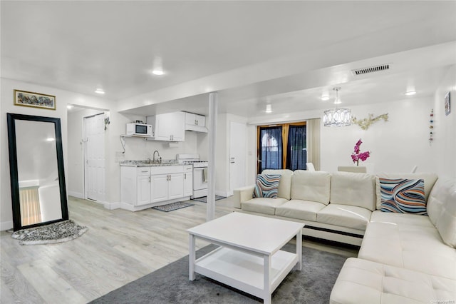 living room featuring light wood finished floors, visible vents, an inviting chandelier, and baseboards