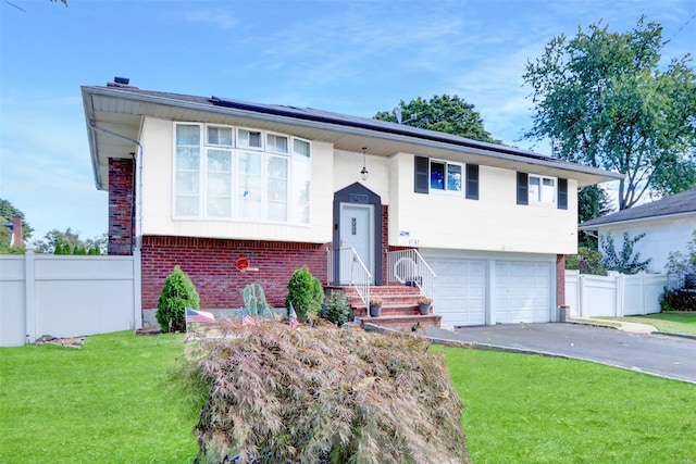 bi-level home featuring a front lawn, aphalt driveway, fence, brick siding, and solar panels