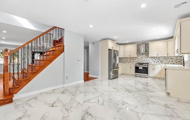 kitchen featuring cream cabinets, wall chimney range hood, sink, appliances with stainless steel finishes, and tasteful backsplash