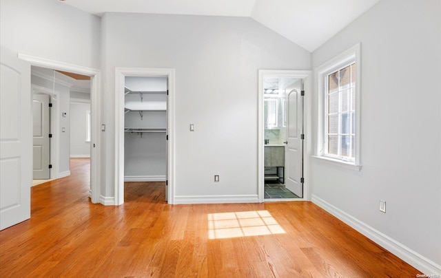 unfurnished bedroom featuring a closet, a spacious closet, ensuite bathroom, and light hardwood / wood-style floors