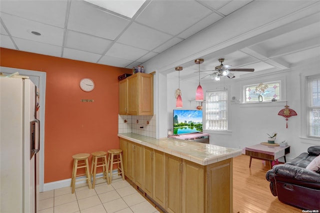 kitchen featuring ceiling fan, white fridge with ice dispenser, kitchen peninsula, tile countertops, and light tile patterned floors