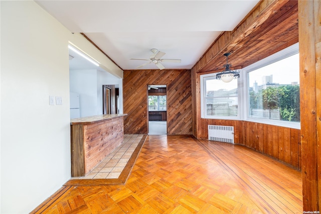 unfurnished living room with radiator heating unit, light parquet floors, ceiling fan, and wood walls