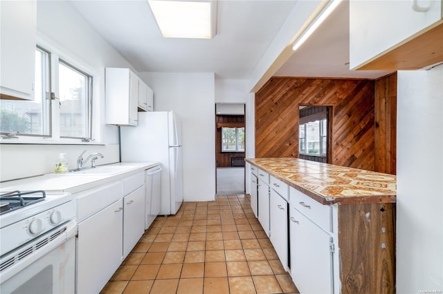 kitchen with a wealth of natural light, white cabinetry, sink, and wooden walls