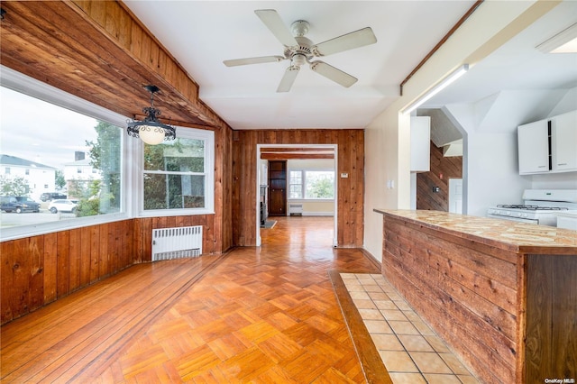 kitchen featuring wooden walls, decorative light fixtures, white range with gas stovetop, radiator heating unit, and white cabinetry