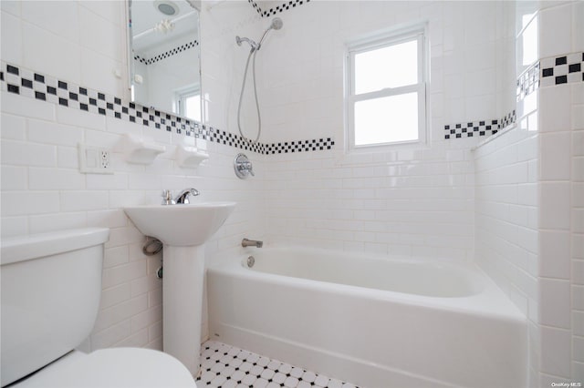 bathroom featuring toilet, tile walls, and tiled shower / bath