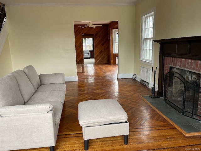 living room with wood walls, dark parquet floors, crown molding, a brick fireplace, and ceiling fan