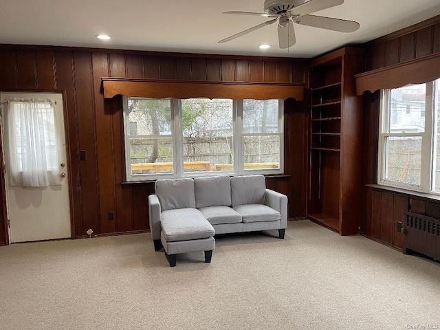 living area featuring ceiling fan, radiator, light carpet, and wooden walls