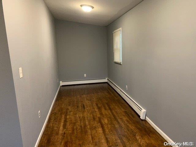 unfurnished room featuring dark hardwood / wood-style flooring and a baseboard heating unit