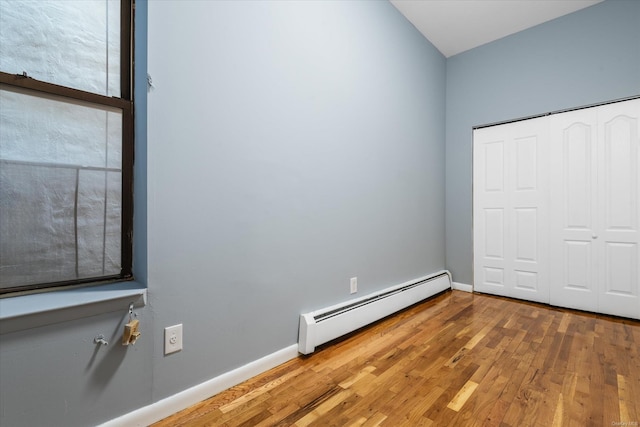 unfurnished bedroom featuring hardwood / wood-style flooring, a closet, and a baseboard heating unit