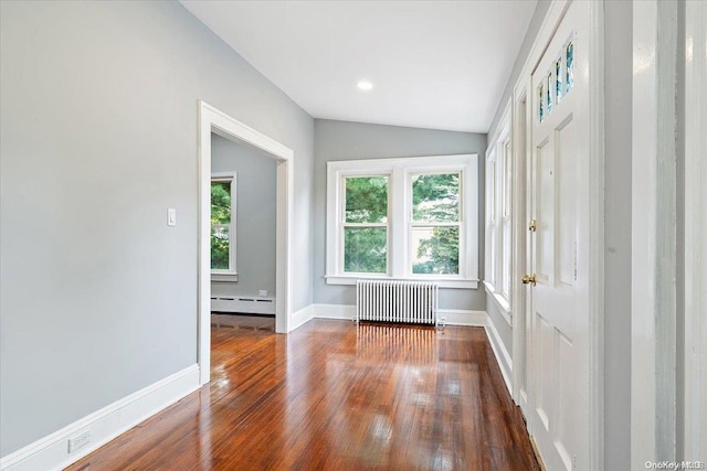 empty room with lofted ceiling, dark hardwood / wood-style floors, radiator heating unit, and a baseboard radiator