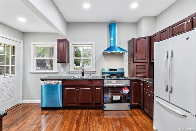 kitchen with dark hardwood / wood-style flooring, wall chimney range hood, stainless steel appliances, and a wealth of natural light