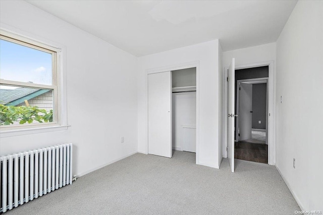 unfurnished bedroom with radiator, a closet, and light colored carpet