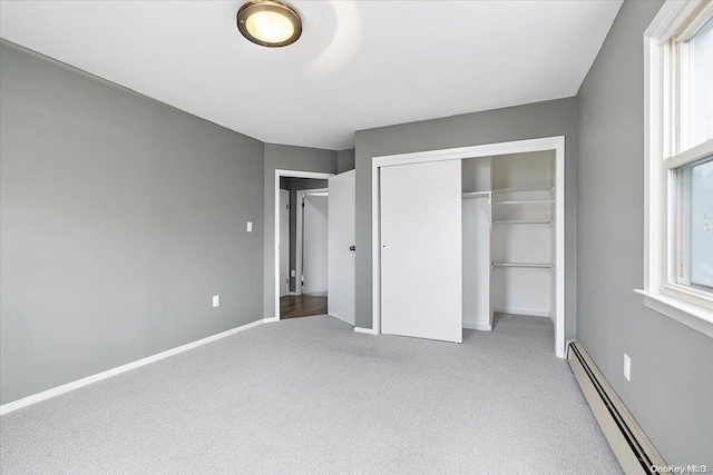 unfurnished bedroom with a closet, carpet floors, multiple windows, and a baseboard heating unit