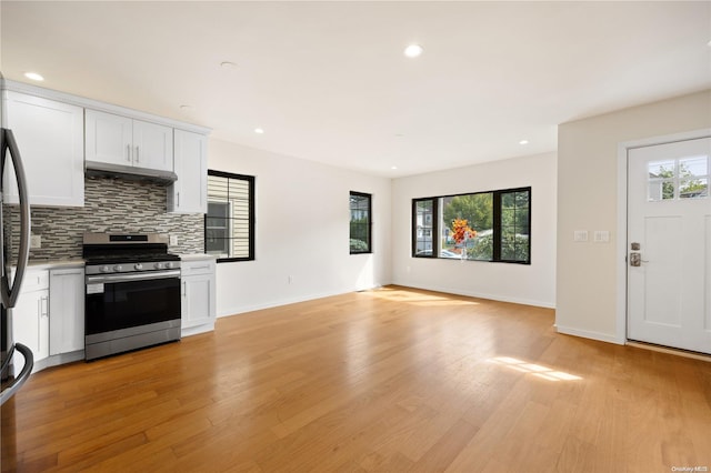 kitchen featuring stainless steel range, tasteful backsplash, light countertops, open floor plan, and white cabinets