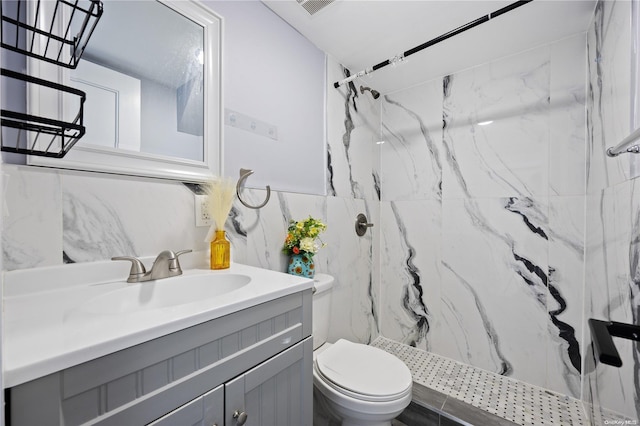 bathroom with a tile shower, vanity, and toilet