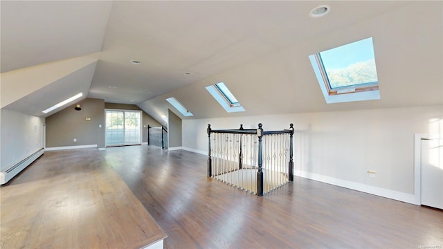 additional living space featuring vaulted ceiling with skylight, wood-type flooring, and a baseboard heating unit