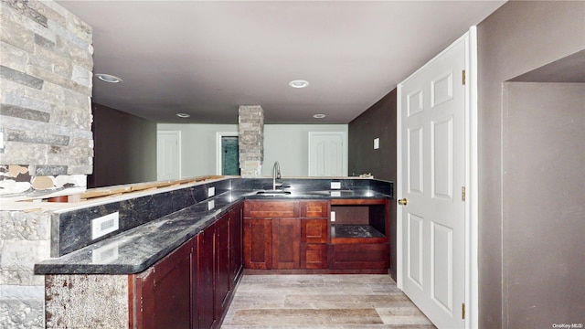 kitchen featuring kitchen peninsula, light hardwood / wood-style flooring, dark stone counters, and sink