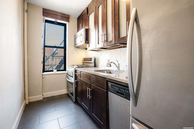 kitchen with sink, decorative backsplash, dark tile patterned floors, appliances with stainless steel finishes, and light stone counters