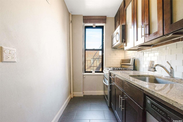 kitchen with sink, stainless steel appliances, light stone counters, backsplash, and dark brown cabinets