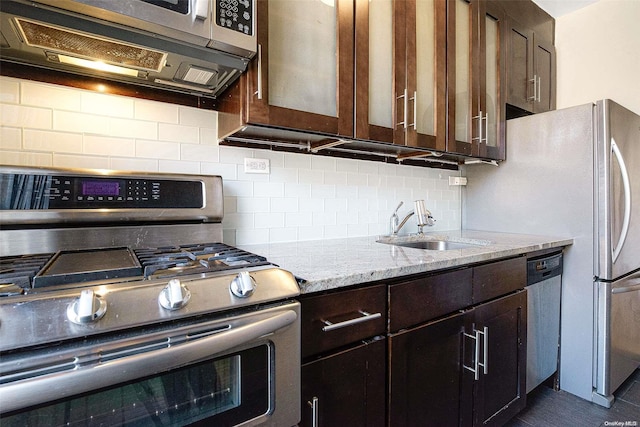 kitchen featuring light stone countertops, decorative backsplash, dark brown cabinets, stainless steel appliances, and sink