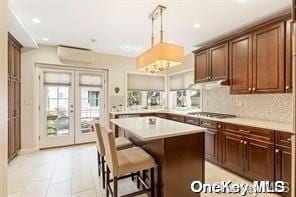 kitchen featuring a wall unit AC, stainless steel gas cooktop, light countertops, a kitchen island, and a kitchen bar