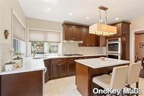 kitchen featuring decorative light fixtures, black stovetop, light countertops, stainless steel double oven, and under cabinet range hood