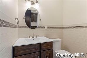 half bath with toilet, tile walls, and vanity