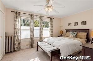 bedroom featuring radiator, light carpet, and ceiling fan