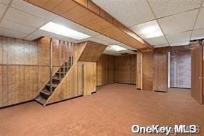 finished basement with light carpet, wood walls, stairway, and a drop ceiling