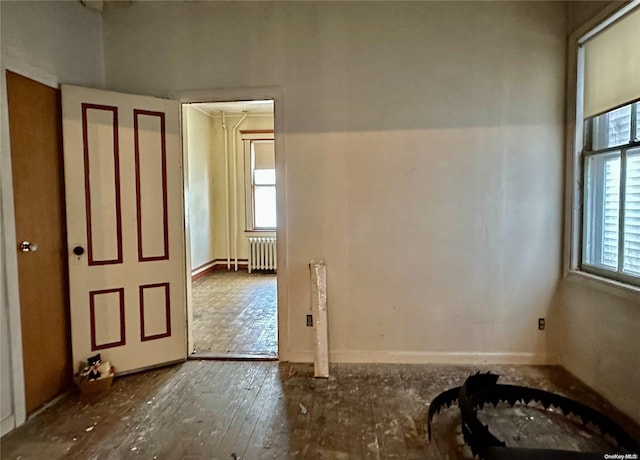 empty room featuring radiator heating unit, a healthy amount of sunlight, and wood-type flooring