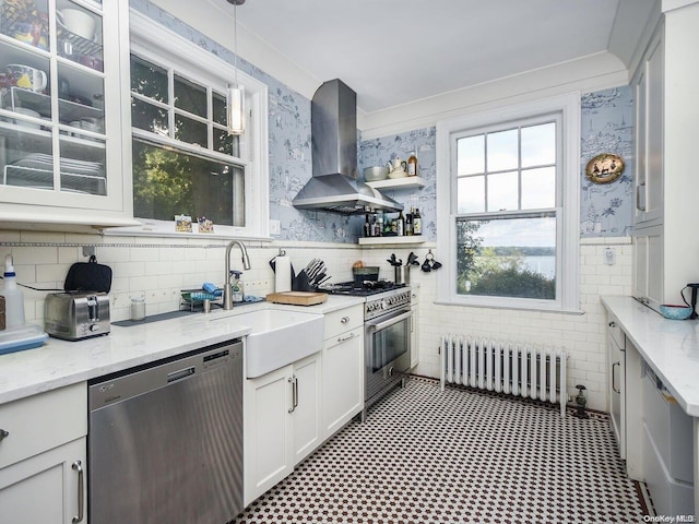 kitchen with ventilation hood, radiator heating unit, appliances with stainless steel finishes, decorative light fixtures, and white cabinetry