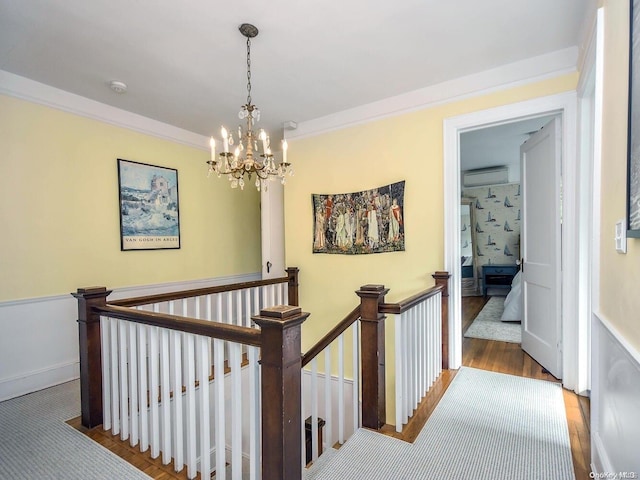 corridor featuring an AC wall unit, hardwood / wood-style floors, ornamental molding, and a notable chandelier