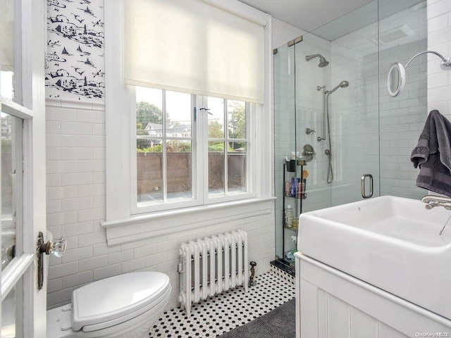 bathroom with tile patterned flooring, radiator, a shower with shower door, and tile walls