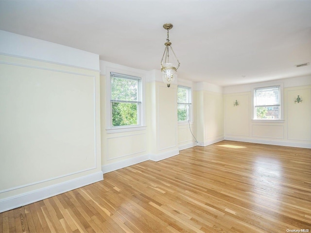 unfurnished room featuring a wealth of natural light, an inviting chandelier, and light wood-type flooring