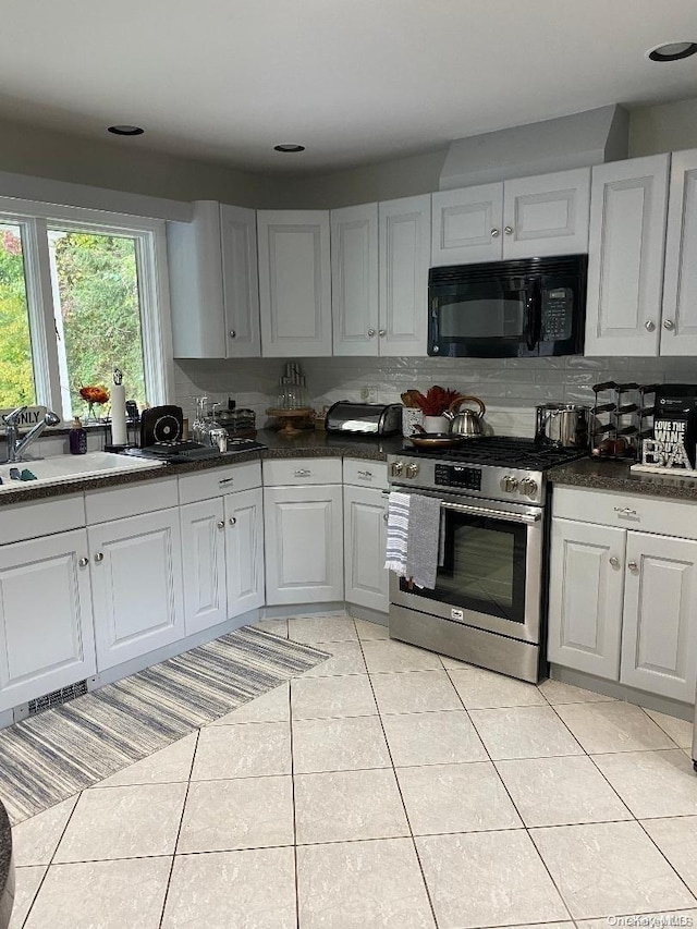 kitchen with decorative backsplash, sink, light tile patterned floors, white cabinets, and stainless steel stove