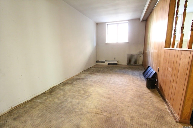 carpeted spare room featuring wooden walls and radiator