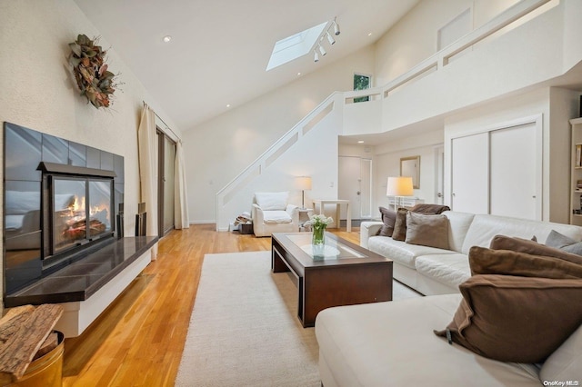 living room featuring light hardwood / wood-style floors, high vaulted ceiling, a skylight, and a tiled fireplace