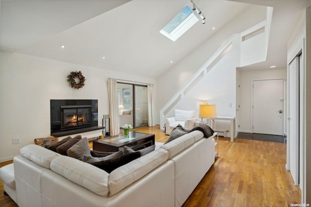 living room with light wood-type flooring, high vaulted ceiling, and a skylight